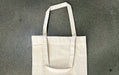 Blank natural cotton tote bag with gusset resting flat on a grey concrete surface
