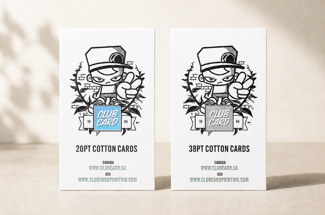 Two printed letterpress cards standing upright on a light beige surface, each showing a black line-art illustration of the Clubcard Mascot character with a hat and the text 'CLUB CARD,' plus quantity and website text. The left card says 20PT cotton cards with blue foil and the right says 38PT cotton cards with iridescent foil.