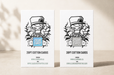 Two printed letterpress cards standing upright on a light beige surface, each showing a black line-art illustration of the Clubcard Mascot character with a hat and the text 'CLUB CARD,' plus quantity and website text. The left card says 20PT cotton cards with blue foil and the right says 38PT cotton cards with iridescent foil.