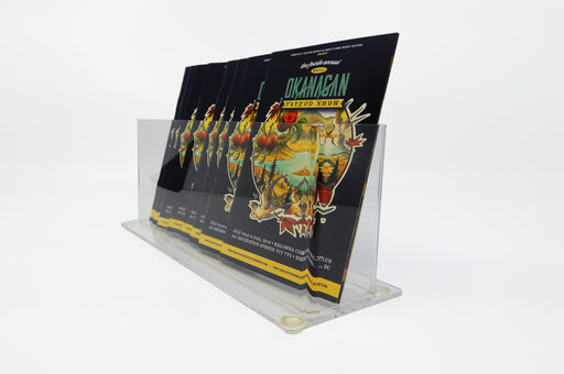 Side of a clear acrylic rack card stand holding 8 saddle stitch booklets for the 2016 Okanagan Tattoo Show.