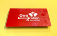 Business cards for One Immigration Consulting on silk laminated 19pt stock | Red background with their logo in the middle | There are travel items like suitcase, passport, and camera around the logo in spot gloss | Clubcard Printing USA